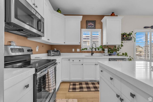 Kitchen featuring white cabinets, light wood finished floors, stainless steel appliances, light countertops, and a sink | Image 9
