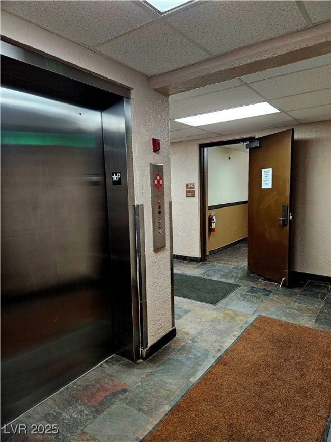 Corridor featuring stone tile flooring, elevator, a textured wall, and a drop ceiling | Image 29