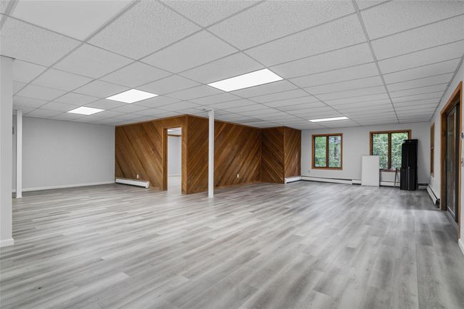 Unfurnished living room with baseboard heating, a drop ceiling, wood walls, and wood finished floors | Image 24