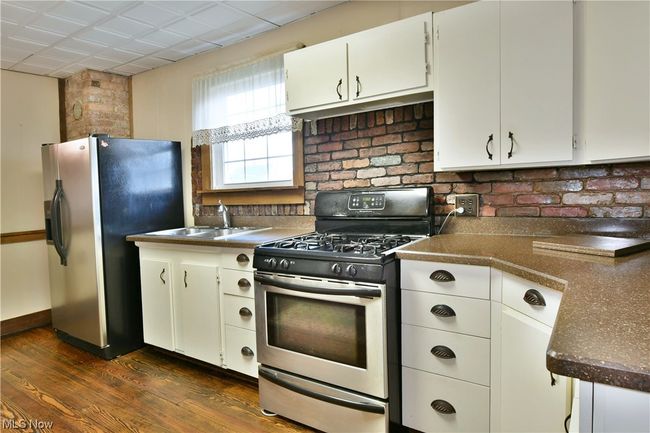 Kitchen featuring white cabinetry, sink, appliances with stainless steel finishes, dark hardwood / wood-style flooring, and brick wall | Image 7