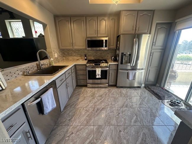 Kitchen featuring appliances with stainless steel finishes, decorative backsplash, light stone countertops, and gray cabinetry | Image 5