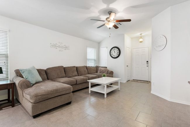 The living room is bright and open with lots of space and opens to the kitchen! It has tall ceilings, a ceiling fan, and tile flooring. | Image 4