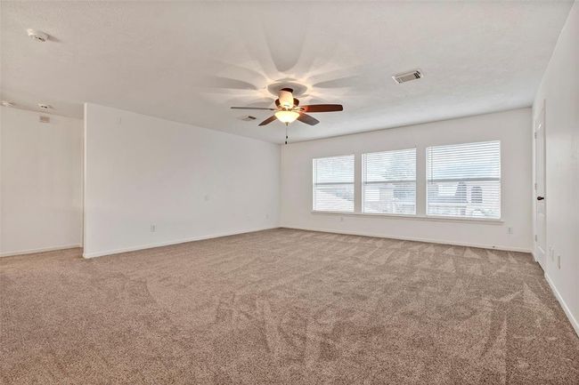This spacious room features neutral-toned carpet and white walls, offering a bright and airy feel. It includes a ceiling fan for comfort and large windows that allow plenty of natural light. | Image 22
