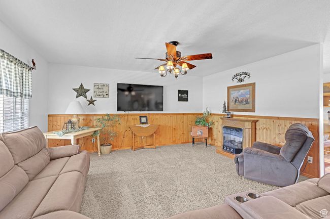 L Living area with wainscoting, wooden walls, carpet, ceiling fan, and a fireplace | Image 4