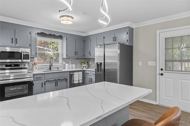 Kitchen quartz counter featuring gray cabinetry, crown molding, appliances with stainless steel finishes, and decorative backsplash | Image 17