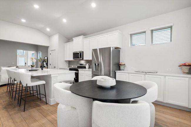 Kitchen with appliances with stainless steel finishes, a kitchen island with sink, a kitchen bar, white cabinetry, and backsplash | Image 6