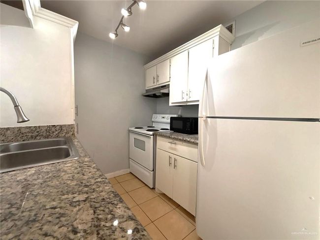 Kitchen featuring light tile patterned floors, white appliances, white cabinetry, under cabinet range hood, and a sink | Image 10