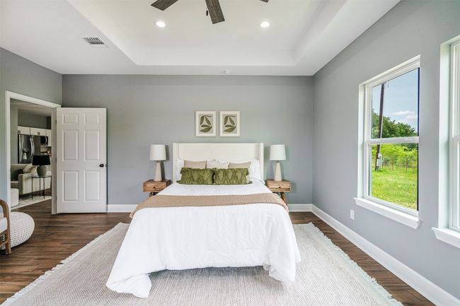 Bedroom with dark wood-style floors, baseboards, stainless steel fridge with ice dispenser, a tray ceiling, and a ceiling fan | Image 14