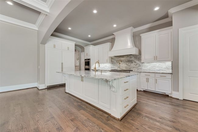 Kitchen with white cabinets, arched walkways, dark wood-type flooring, and custom range hood | Image 11