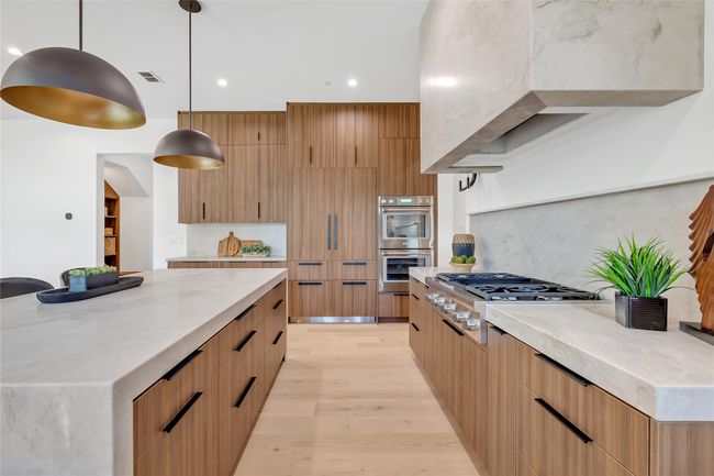 Kitchen featuring appliances with stainless steel finishes, modern cabinets, backsplash, light wood-type flooring, and light stone countertops | Image 9