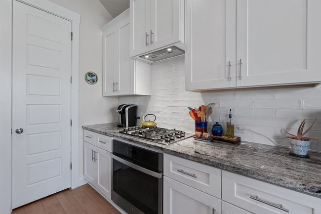 Kitchen featuring appliances with stainless steel finishes, under cabinet range hood, white cabinets, and stone counters | Image 5