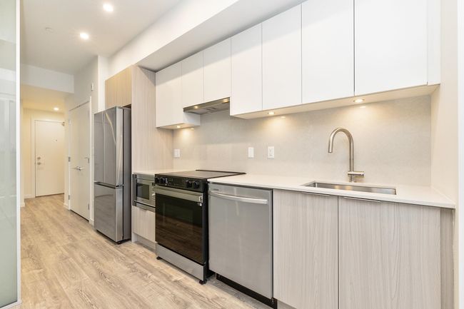Kitchen with stainless steel appliances, a sink, light wood-type flooring, modern cabinets, and light countertops | Image 9
