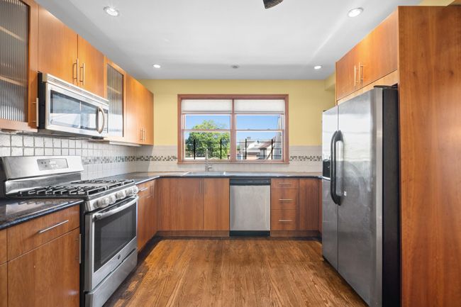 Kitchen featuring appliances with stainless steel finishes, dark wood finished floors, brown cabinetry, recessed lighting, and glass insert cabinets | Image 12