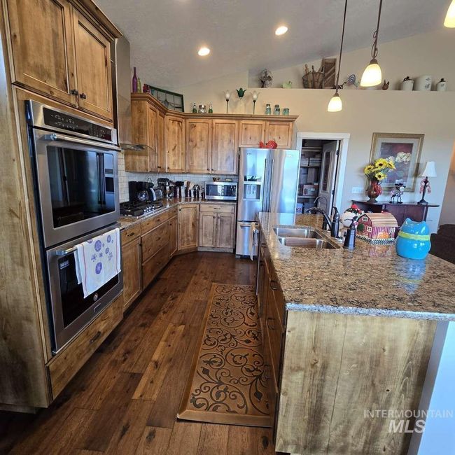 Kitchen with appliances with stainless steel finishes, vaulted ceiling, a kitchen island with sink, light stone counters, and dark wood-style floors | Image 8