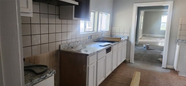 Kitchen with exhaust hood, white cabinetry, light countertops, and decorative backsplash | Image 9