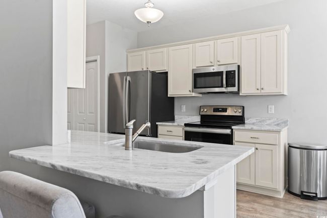 Kitchen with a breakfast bar area, appliances with stainless steel finishes, a sink, a peninsula, and light wood-style flooring | Image 13