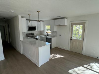 Kitchen featuring kitchen peninsula, white cabinets, sink, decorative light fixtures, and stainless steel appliances | Image 3