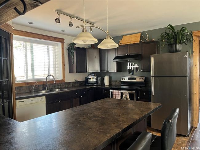 Kitchen with a sink, dark countertops, stainless steel appliances, under cabinet range hood, and decorative light fixtures | Image 9