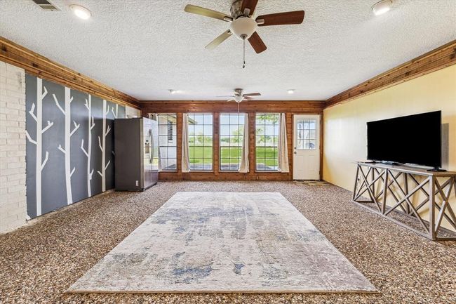 The sunroom is through the barn doors just off the main living area, offering a wall of windows to bring in natural lighting, pebble flooring, wood trim and access to the outdoor patio, making this space ideal for additional living area, game room or a second living area | Image 22