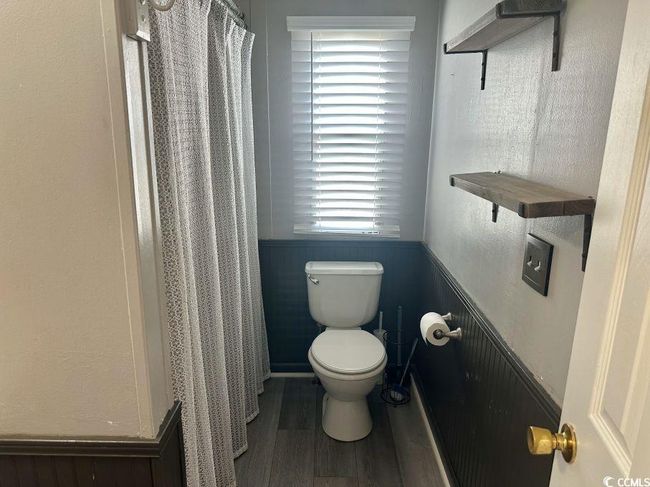 Bathroom with a wainscoted wall, toilet, wood finished floors, and a shower with shower curtain | Image 23