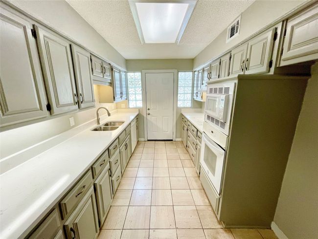 Kitchen featuring a textured ceiling, a sink, white appliances, light countertops, and visible vents | Image 7
