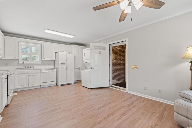 Kitchen with white appliances, stacked washer and clothes dryer, light countertops, light wood-style flooring, and white cabinetry | Image 30