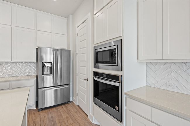 Kitchen with stainless steel appliances, white cabinets, light wood-type flooring, light countertops, and tasteful backsplash | Image 10