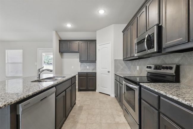 Kitchen with appliances with stainless steel finishes, a sink, light stone countertops, backsplash, and recessed lighting | Image 11