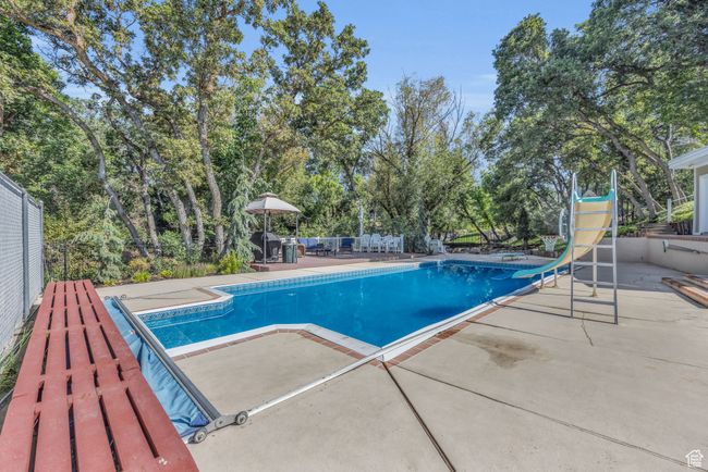 Swimming pool featuring a patio area, a water slide, and view of scattered trees | Image 35