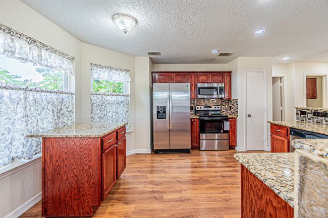 Kitchen featuring stainless steel appliances, light wood-style flooring, a textured ceiling, tasteful backsplash, and light stone countertops | Image 13
