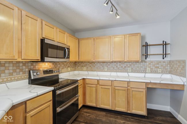 kitchen featuring appliances with stainless steel finishes, light brown cabinets, dark wood-style flooring, backsplash, and a textured ceiling | Image 30