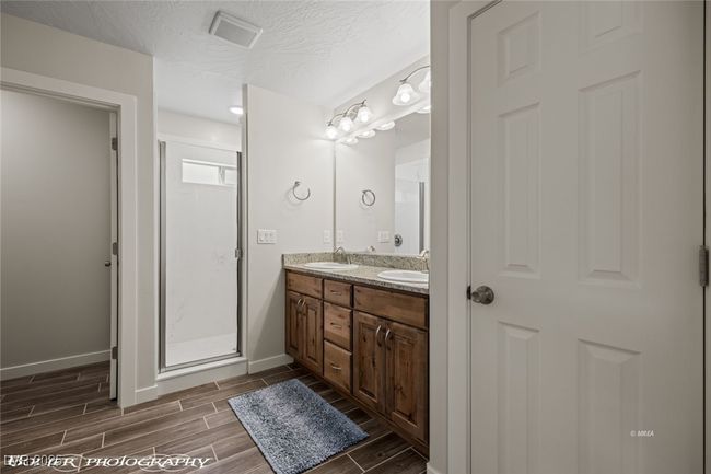Full bath with wood tiled floors, baseboards, double vanity, a shower stall, and a textured ceiling | Image 39