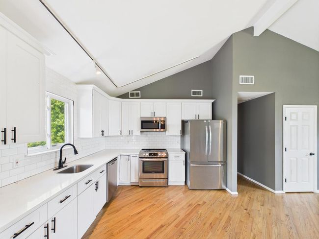 Kitchen featuring stainless steel appliances, light wood finished floors, white cabinets, tasteful backsplash, and beam ceiling | Image 5