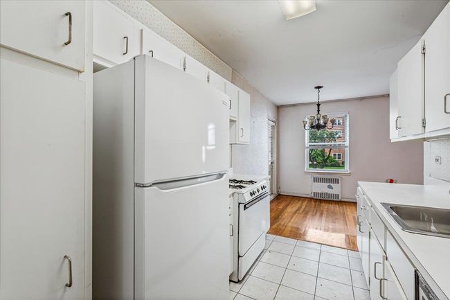 Kitchen with white appliances, radiator heating unit, light countertops, white cabinetry, and a chandelier | Image 7