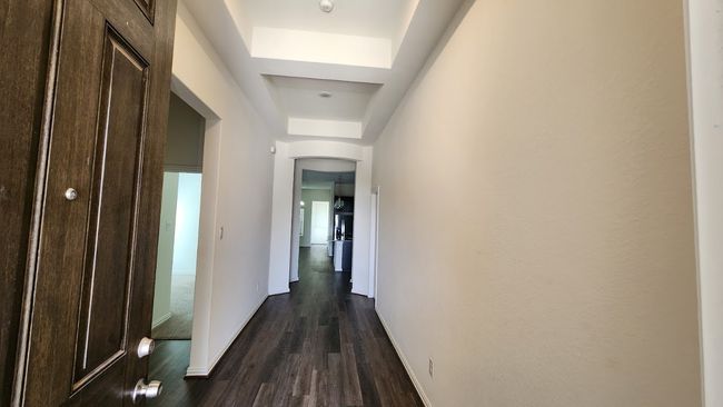Hall featuring a tray ceiling, dark wood-style flooring, baseboards, and arched walkways | Image 4