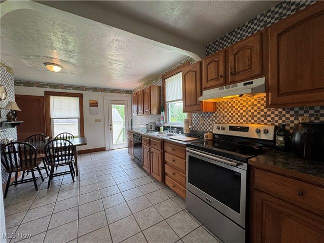 Kitchen featuring electric stove, under cabinet range hood, a textured ceiling, dishwasher, and a sink | Image 9