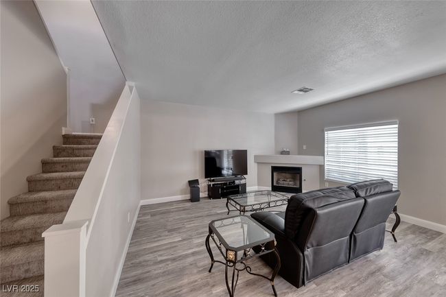 Living area with a textured ceiling, stairs, wood finished floors, and a fireplace | Image 6