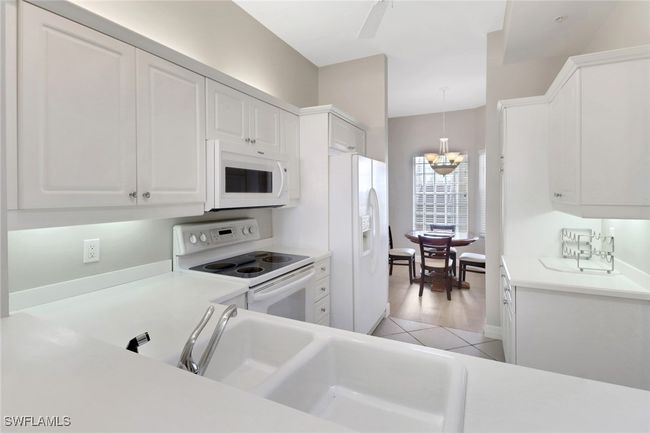 Kitchen featuring white appliances, white cabinets, light countertops, and decorative light fixtures | Image 5