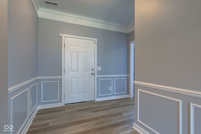 foyer entrance featuring crown molding, wood finished floors, a decorative wall, a wainscoted wall, and a textured ceiling | Image 14