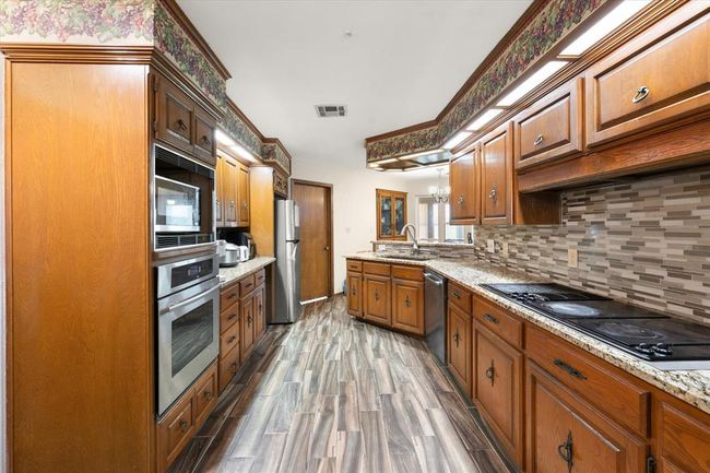 Kitchen featuring appliances with stainless steel finishes, a sink, backsplash, and brown cabinets | Image 12