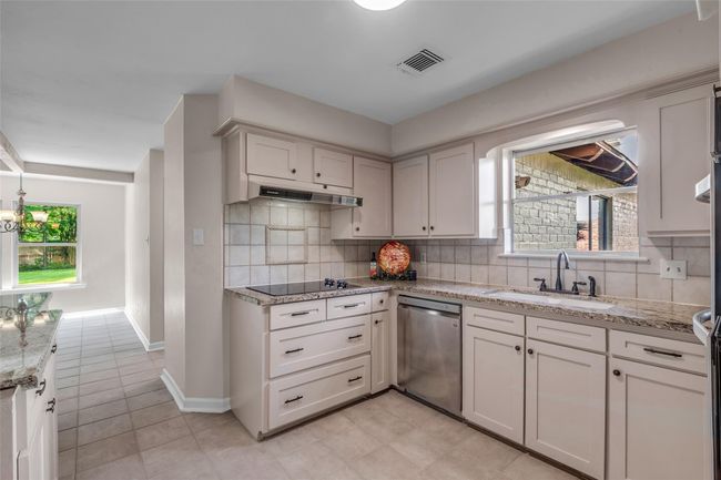 This kitchen features light cabinetry with granite countertops and a tile backsplash. It includes modern appliances and opens to a bright dining area with large windows overlooking the breakfast room and the backyard. | Image 20
