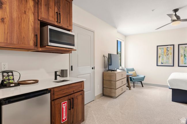 Kitchen with stainless steel appliances, light colored carpet, a sink, brown cabinetry, and baseboards | Image 30