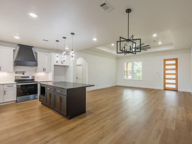 This gourmet kitchen boasts sleek black and white cabinetry, bold pendant lighting, a large center island with bar seating, and a custom range hood—combining style and function in one impressive space. | Image 12