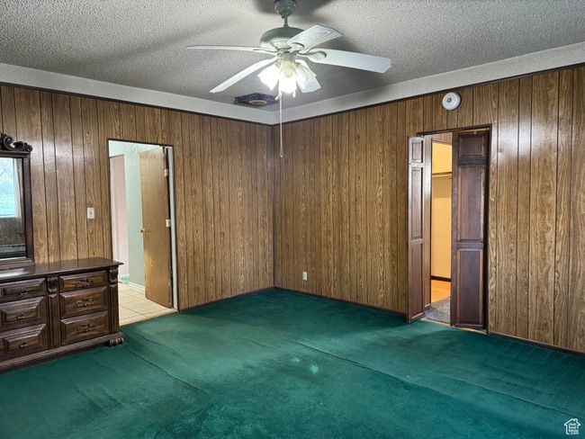 Unfurnished bedroom with light carpet, wood walls, a textured ceiling, and ceiling fan | Image 11