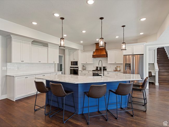 Kitchen with stainless steel appliances, custom exhaust hood, a large island, white cabinets, and decorative backsplash | Image 8