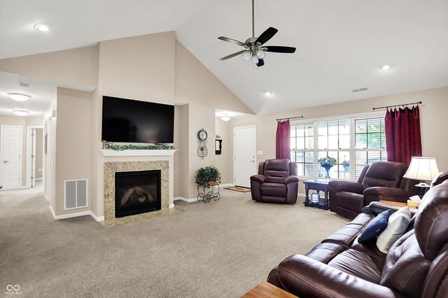 Carpeted living room featuring high vaulted ceiling, ceiling fan, and a fireplace | Image 8