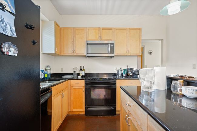 Kitchen featuring black appliances, light brown cabinets, concrete floors, and dark stone countertops | Image 7