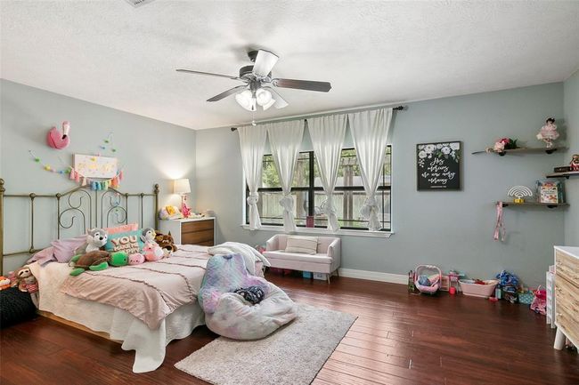 This cozy bedroom features hardwood floors, a large window with sheer curtains for natural light, and a ceiling fan. It's decorated with whimsical elements, making it ideal for a child's room. The space includes a twin bed, plush toys, and ample floor space for play. | Image 34