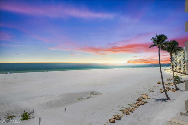 The beach stretches endlessly beneath a sky ablaze with sunset colors—fiery oranges, pinks, and purples melting into the calm Gulf waters. | Image 31