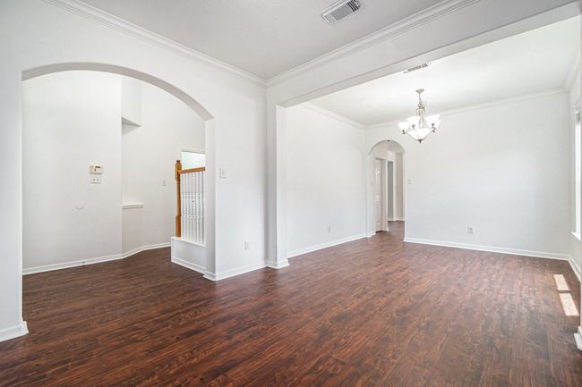 A look at the living and rooms off the kitchen and main entrance. The features elegant flooring, bright white walls, and modern crown molding. It includes a stylish chandelier and archways leading to additional spaces, creating a warm and inviting atmosphere. | Image 5